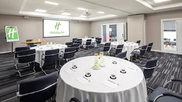 A conference room with multiple tables, chairs, and a projector screen displaying "Holiday Inn".