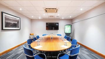 A conference room with a long table, blue chairs, a projector screen, and a framed picture on the wall.