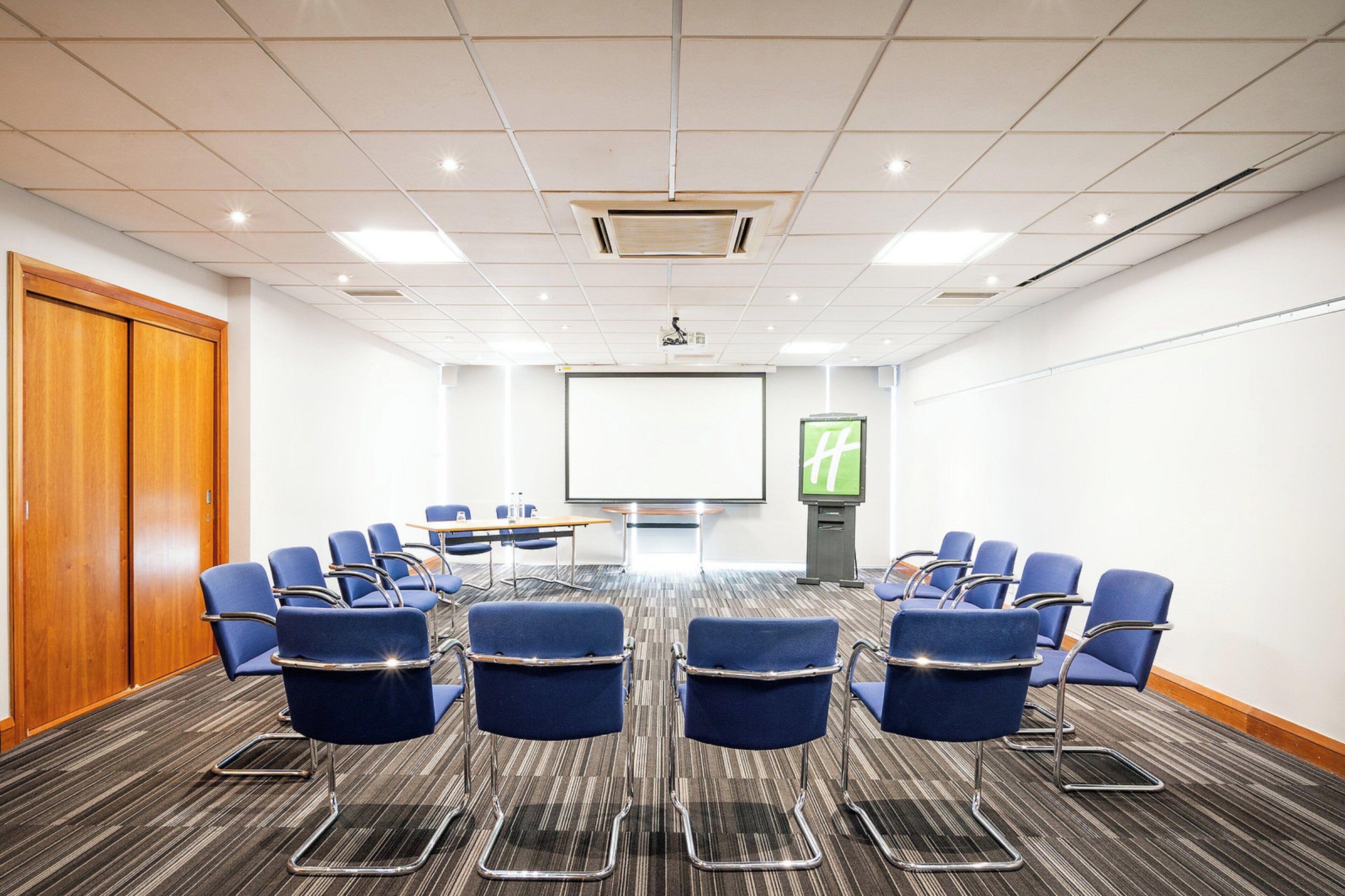 A conference room with a large screen, rows of chairs, and a podium.