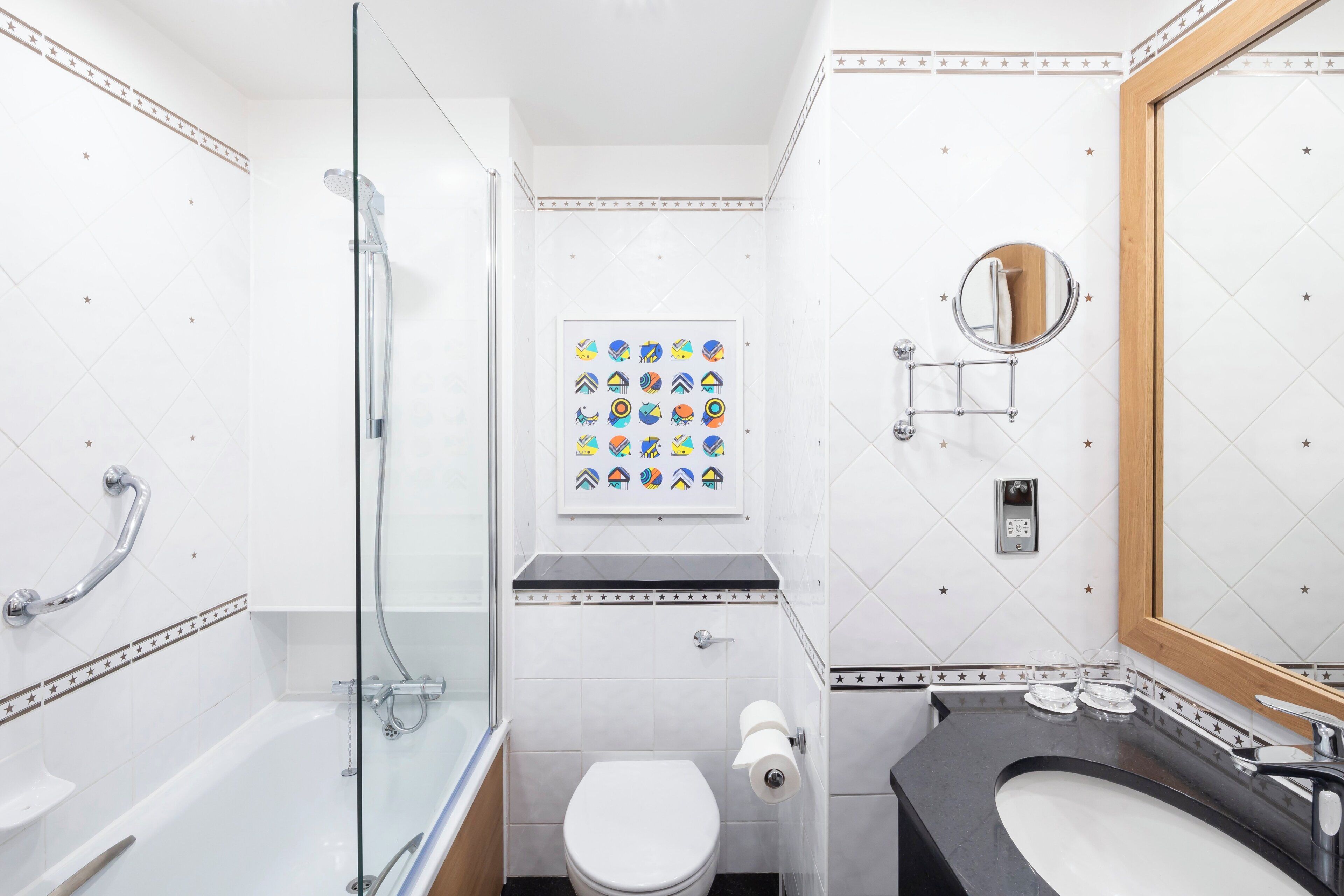 Une salle de bain avec une douche à parois de verre, des toilettes, un lavabo avec un miroir et un porte-rouleau de papier toilette fixé au mur.