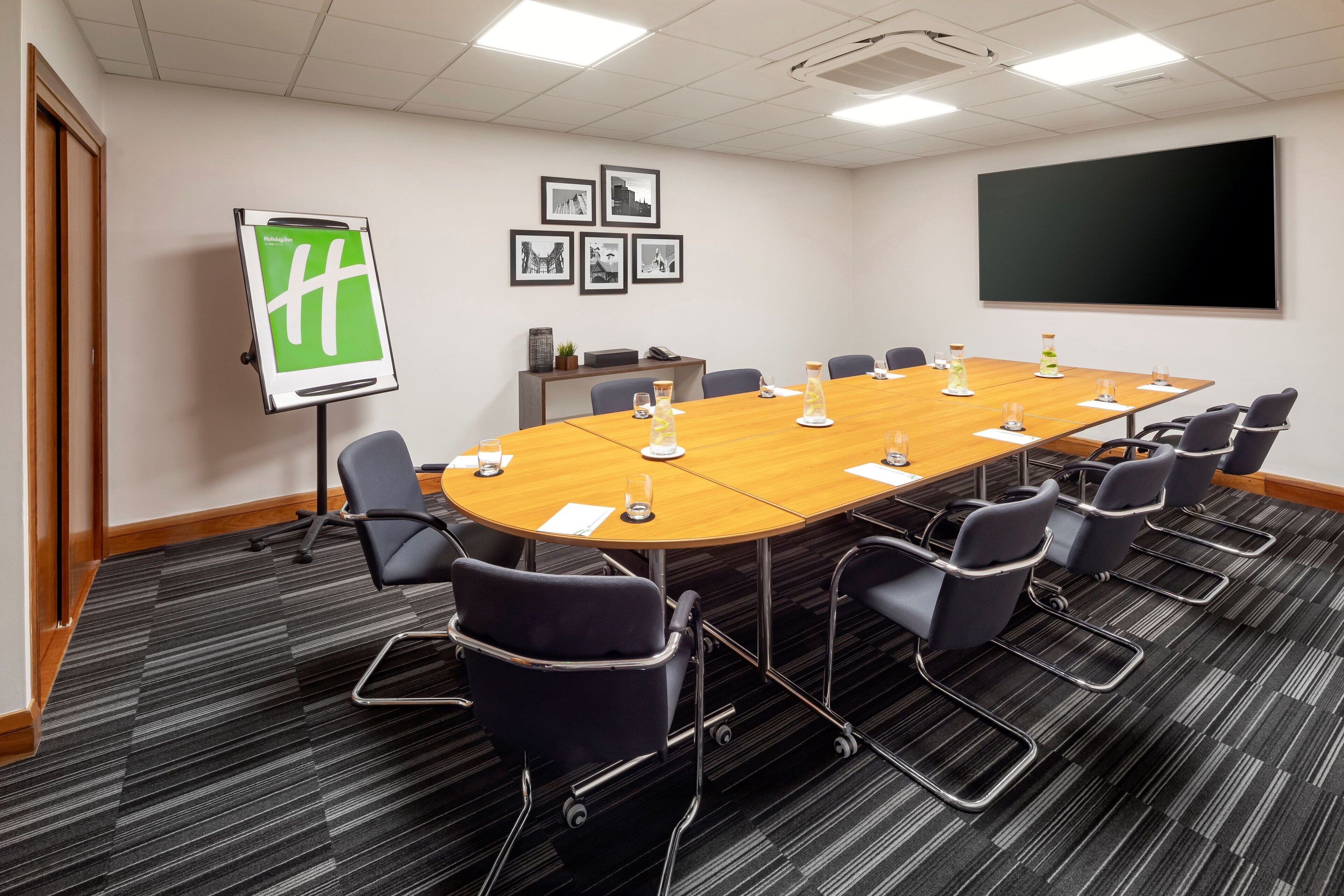 A conference room with a long table, chairs, a projector screen, and framed pictures on the wall.