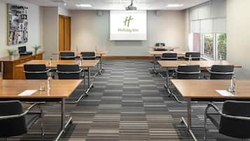A conference room with a large screen displaying the Holiday Inn logo, multiple tables with chairs, and a carpeted floor.