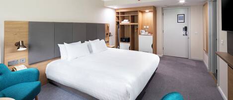 A hotel room with a large bed, a desk, a chair, a TV, and a wardrobe.