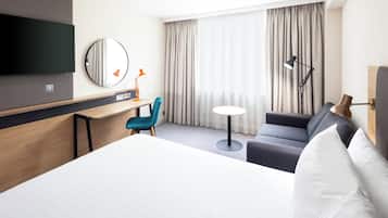Una habitación de hotel con cama, escritorio, silla, televisor y ventana con cortinas.