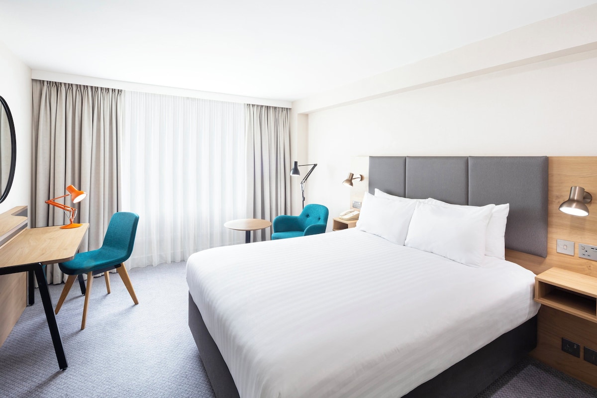 Una habitación de hotel con una cama grande, dos sillas, un escritorio y una mesita.
