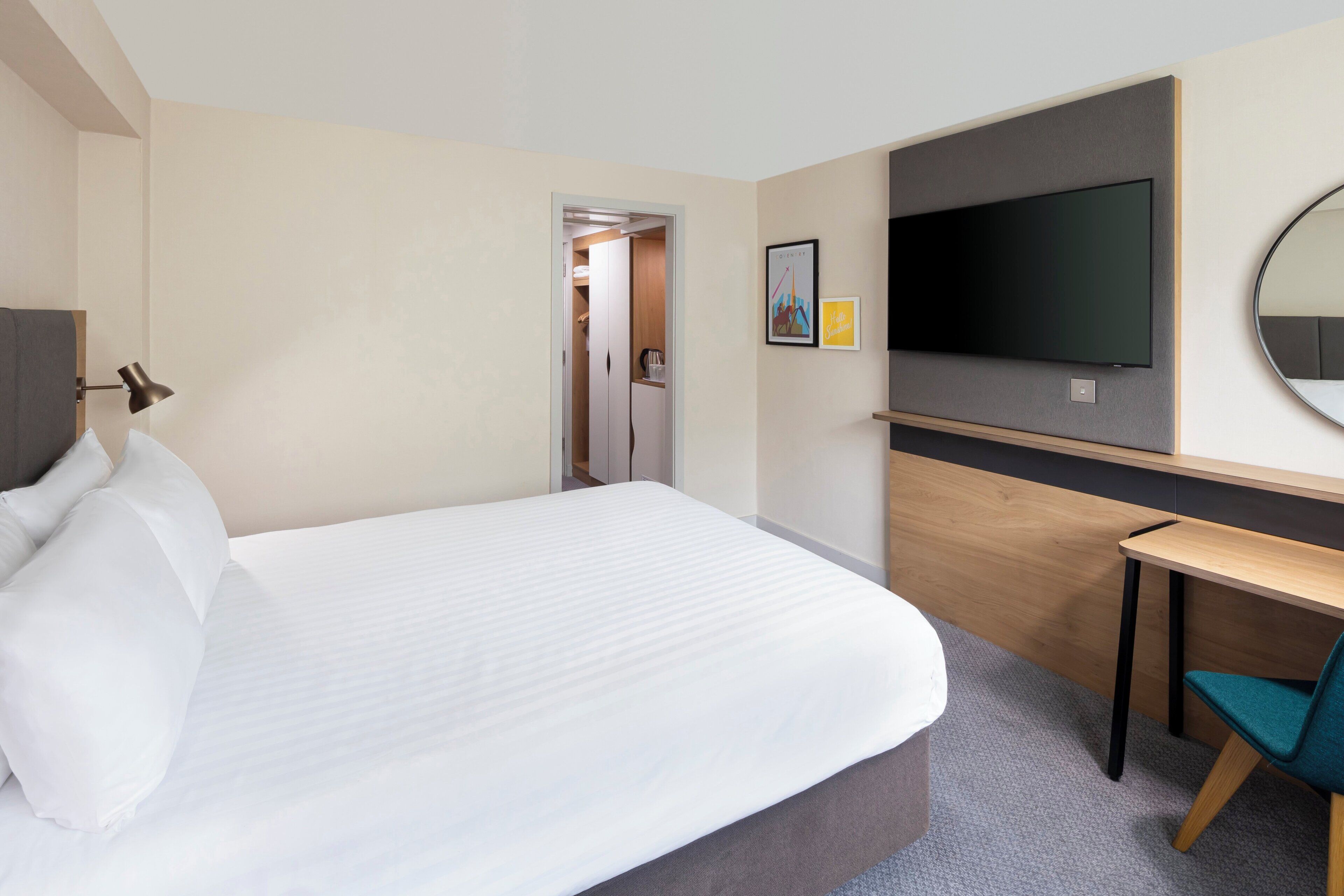 A hotel room with a bed, a desk, a television, and a mirror.