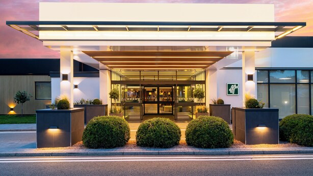 A modern hotel entrance with a covered walkway, glass doors, and well-lit surroundings. - Holiday Inn Coventry M6, Jct.2 by IHG (Coventry)