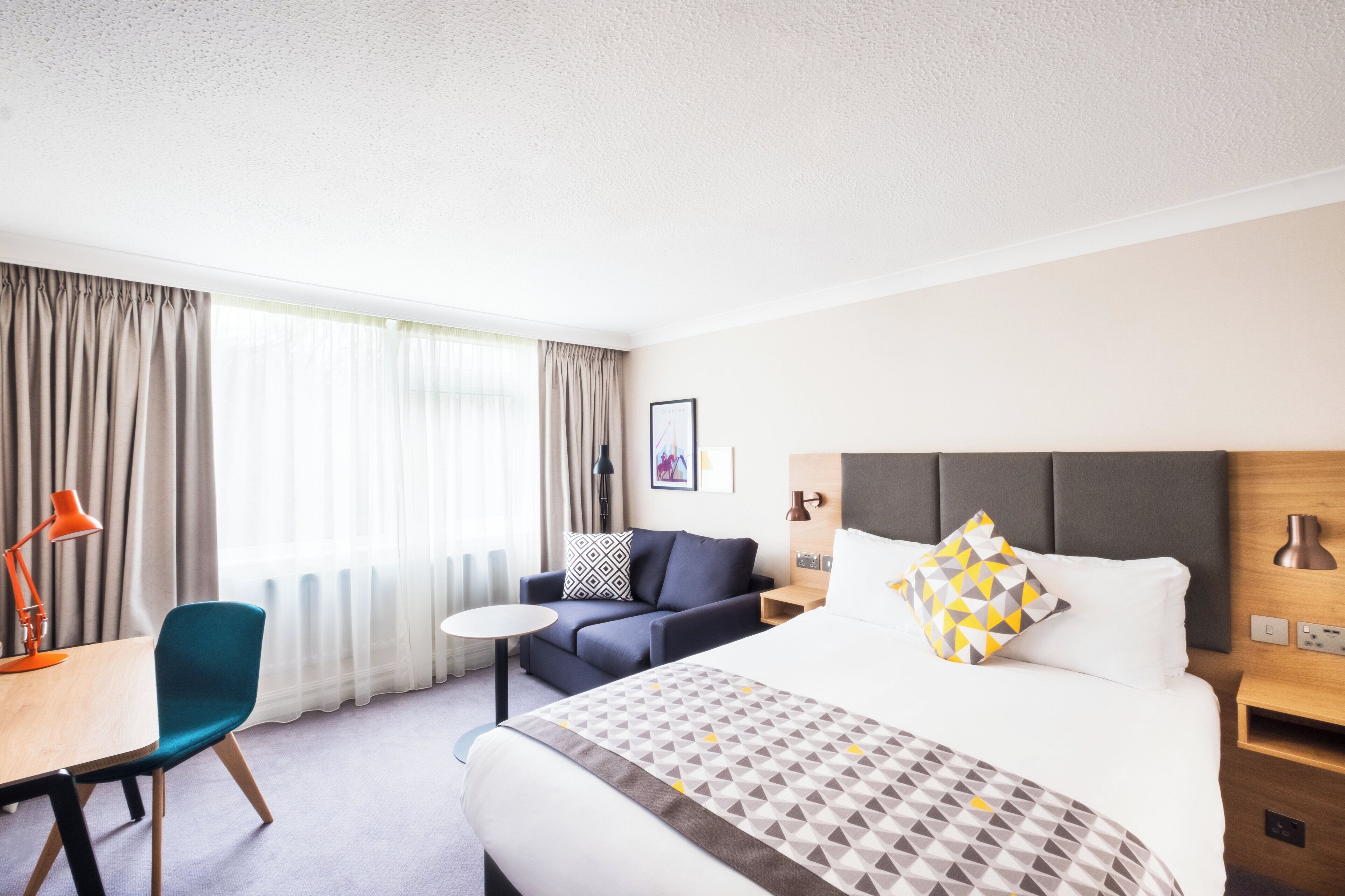 Una habitación de hotel con cama, escritorio, silla y mesita de noche.