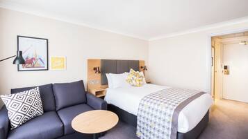 A hotel room with a bed, a sofa, a small table, and a nightstand.