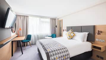 A hotel room with a bed, desk, chair, TV, and a window with curtains.