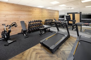 Un gimnasio con cintas de correr, elípticas, bancos de pesas y mancuernas.