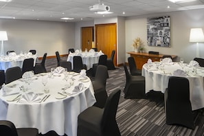 Un salón de conferencias con varias mesas redondas dispuestas para comidas, equipado con sillas, manteles y cubiertos.