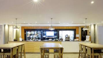 A modern bar area with wooden tables and chairs, a counter with a variety of bottles, and a large screen.