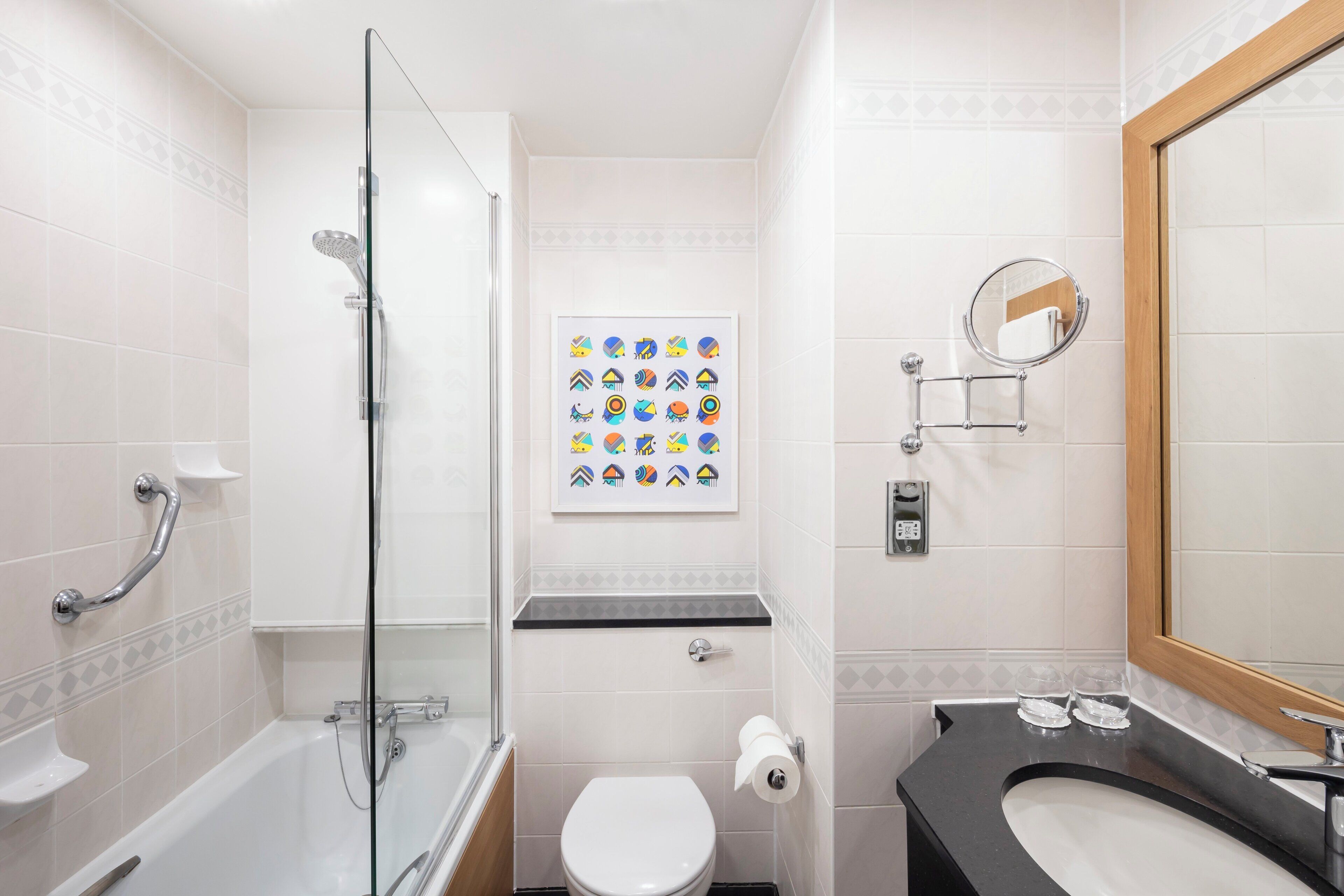 A bathroom with a glass-enclosed shower, a toilet, a sink with a mirror, and a framed artwork on the wall.
