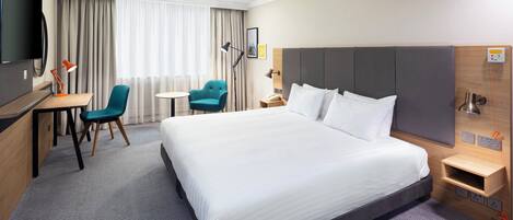 A hotel room with a large bed, a desk, a chair, a TV, and a window with curtains.
