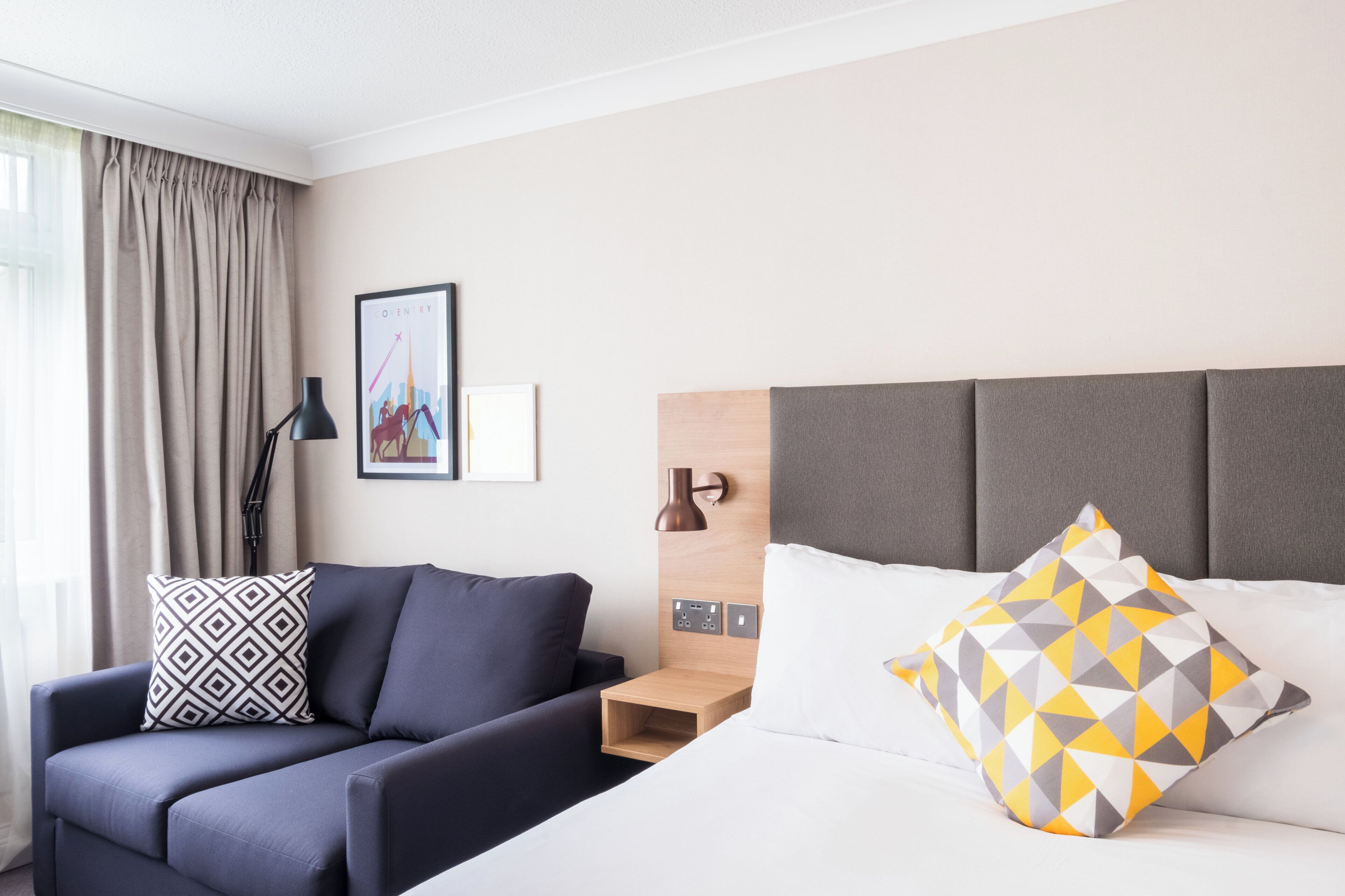 A hotel room with a bed, a desk, a chair, and a sofa.