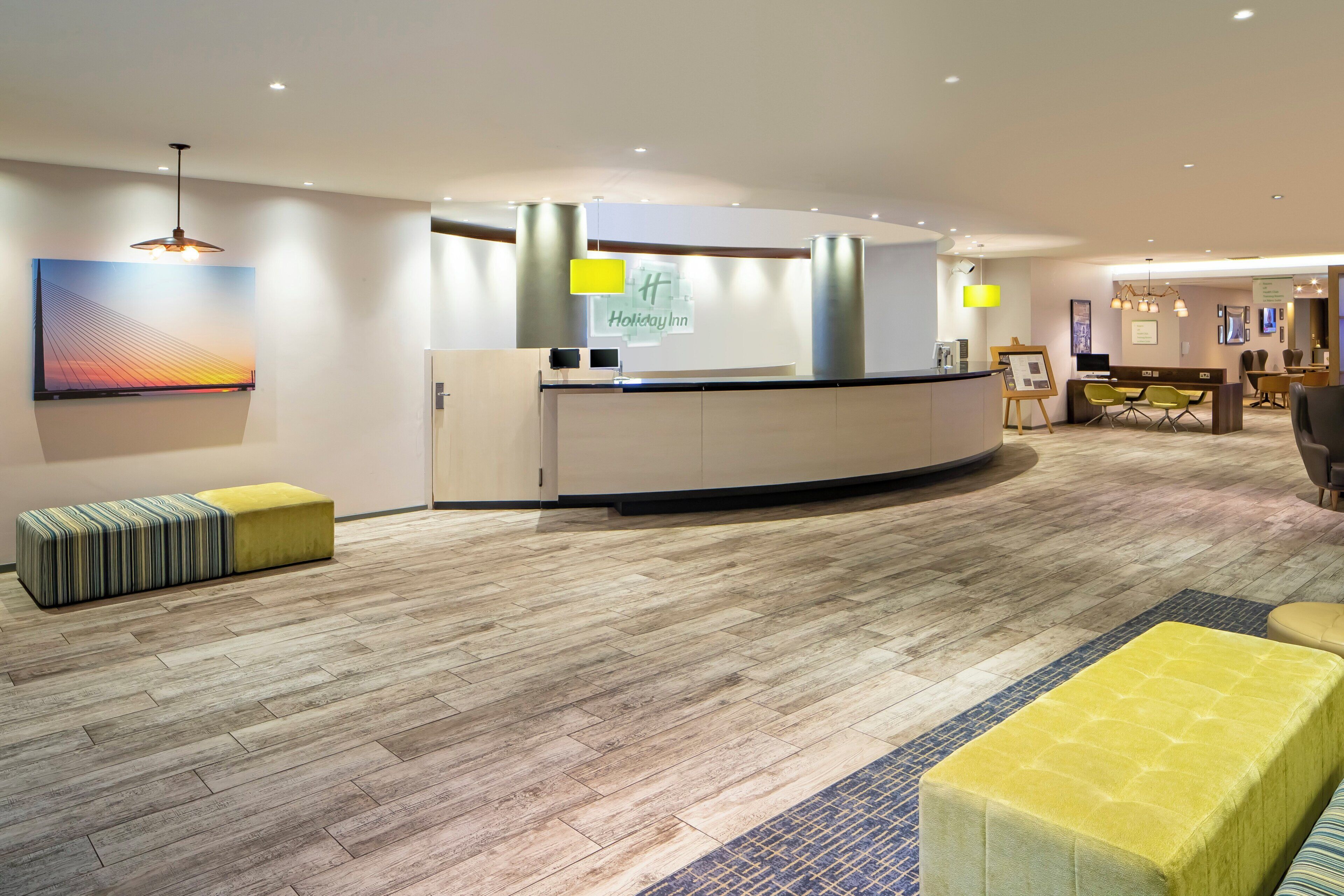 A hotel reception area with a reception desk, a large painting on the wall, and a seating area with ottomans.
