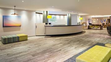 A hotel reception area with a reception desk, a large painting on the wall, and a seating area with ottomans.