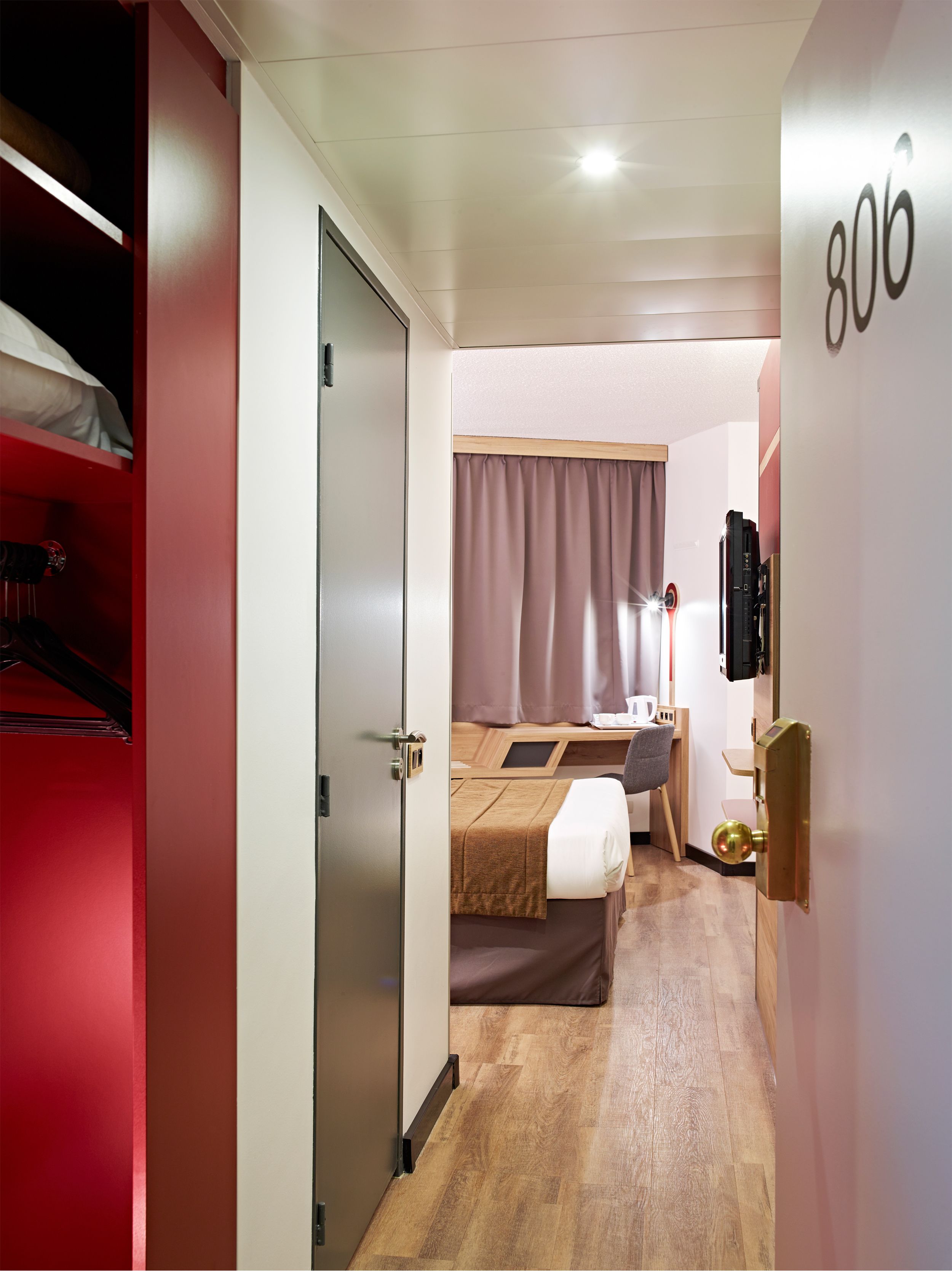 A hotel room with a bed, a desk, a wardrobe, and a door with the number 806.