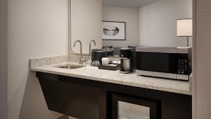 A modern kitchenette with a built-in sink, a coffee maker, a microwave, and a small cabinet.