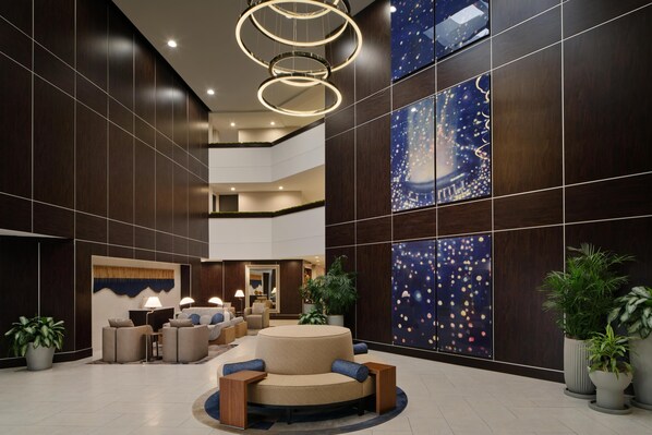 A modern lobby with a central seating area, a large artwork on the wall, and a ceiling with circular light fixtures.