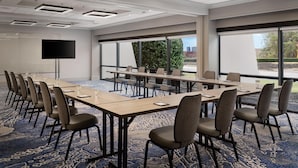 A conference room with a long table, chairs, a projector screen, and a large window with a view of greenery.