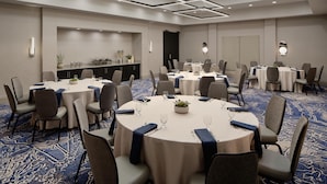 A conference room with round tables, chairs, and a carpeted floor.