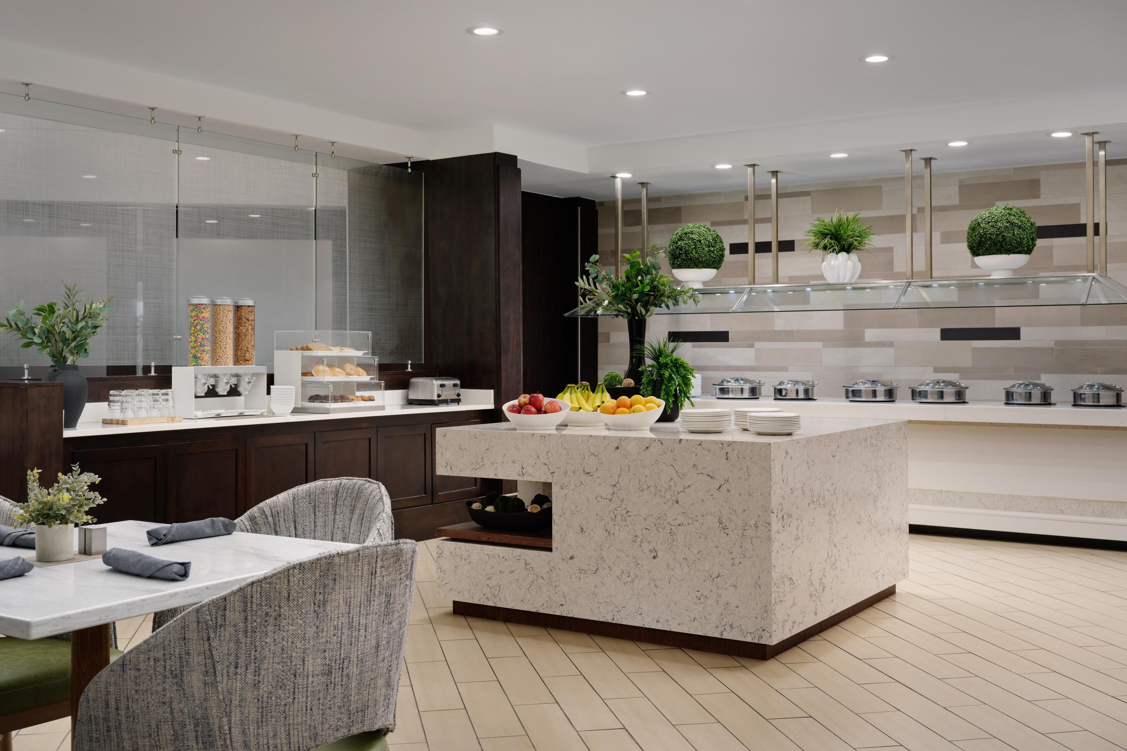 A modern kitchen with a marble countertop, a dining area with a chair, and a glass partition.