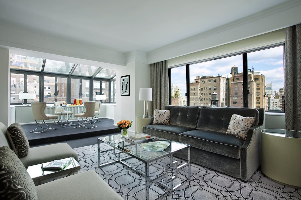 A modern hotel room with a sofa, coffee table, and dining area.