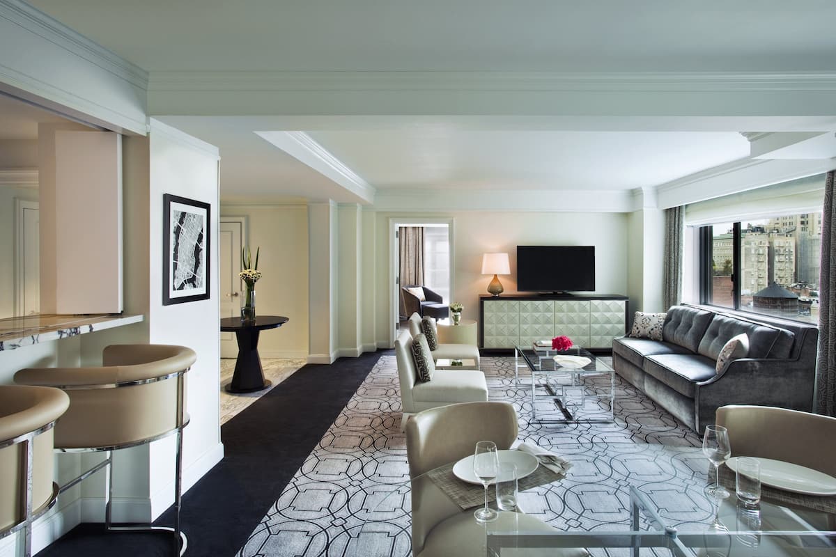 A hotel room with a living area, dining space, and a TV.