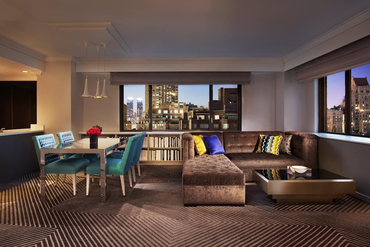A modern living room with a city view, a dining area, and a bookshelf.