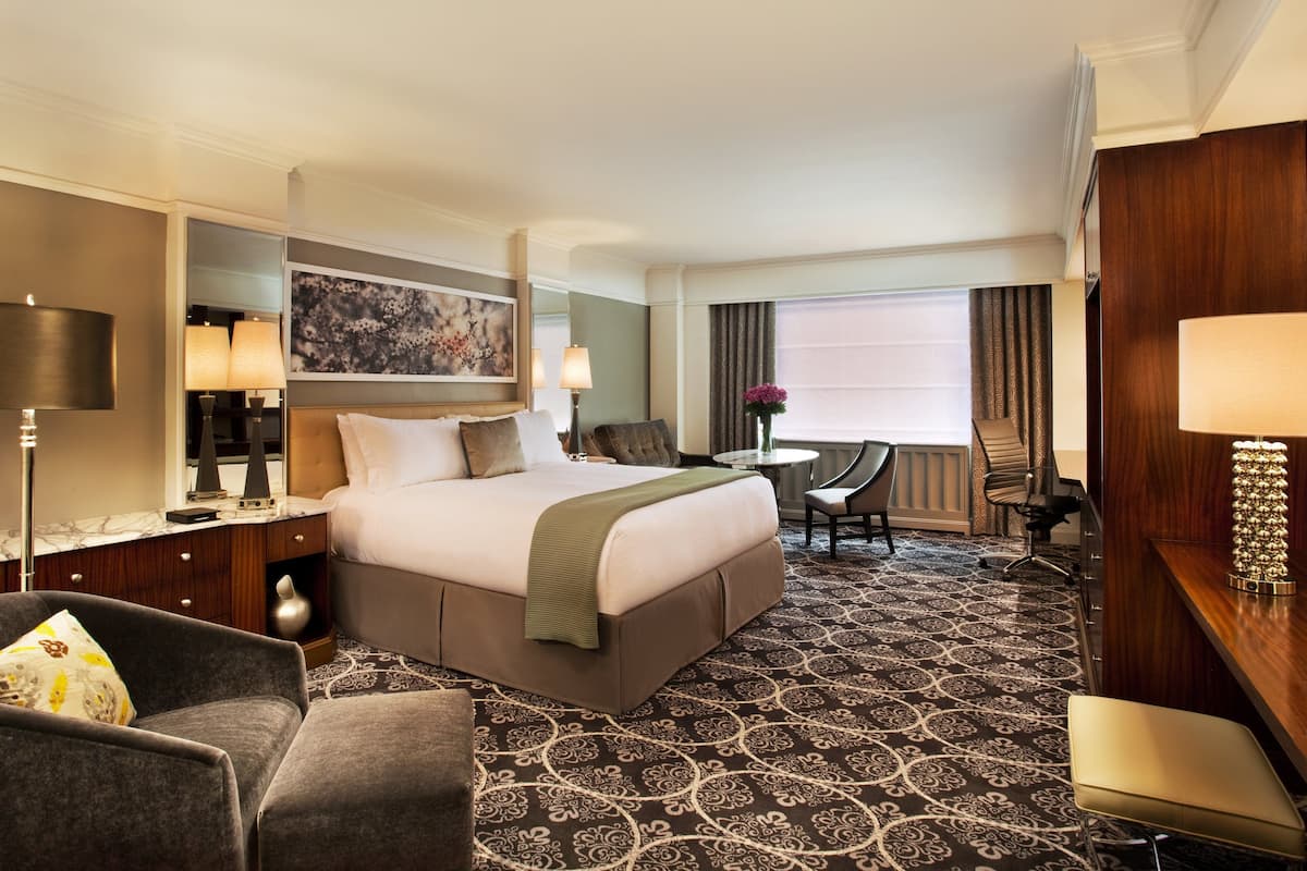 A hotel room with a large bed, a desk, a chair, a lamp, and a painting on the wall.