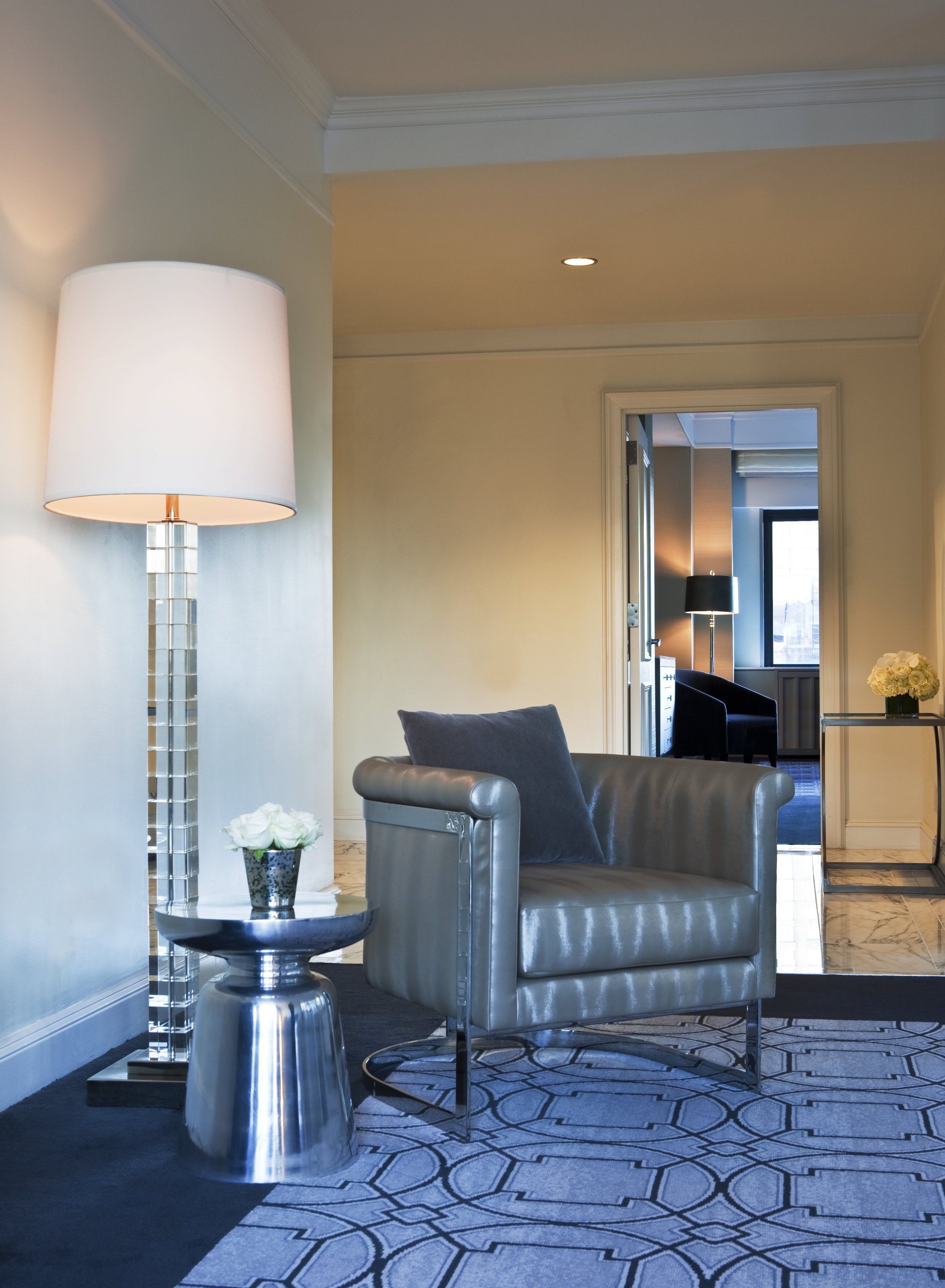 A modern hotel lobby with a leather armchair, a tall floor lamp, and a patterned carpet.