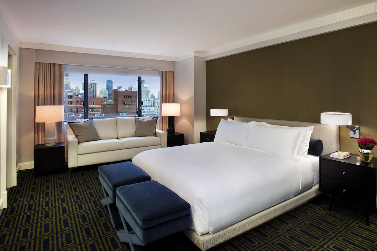 A hotel room with a large bed, a sofa, and a view of a cityscape.