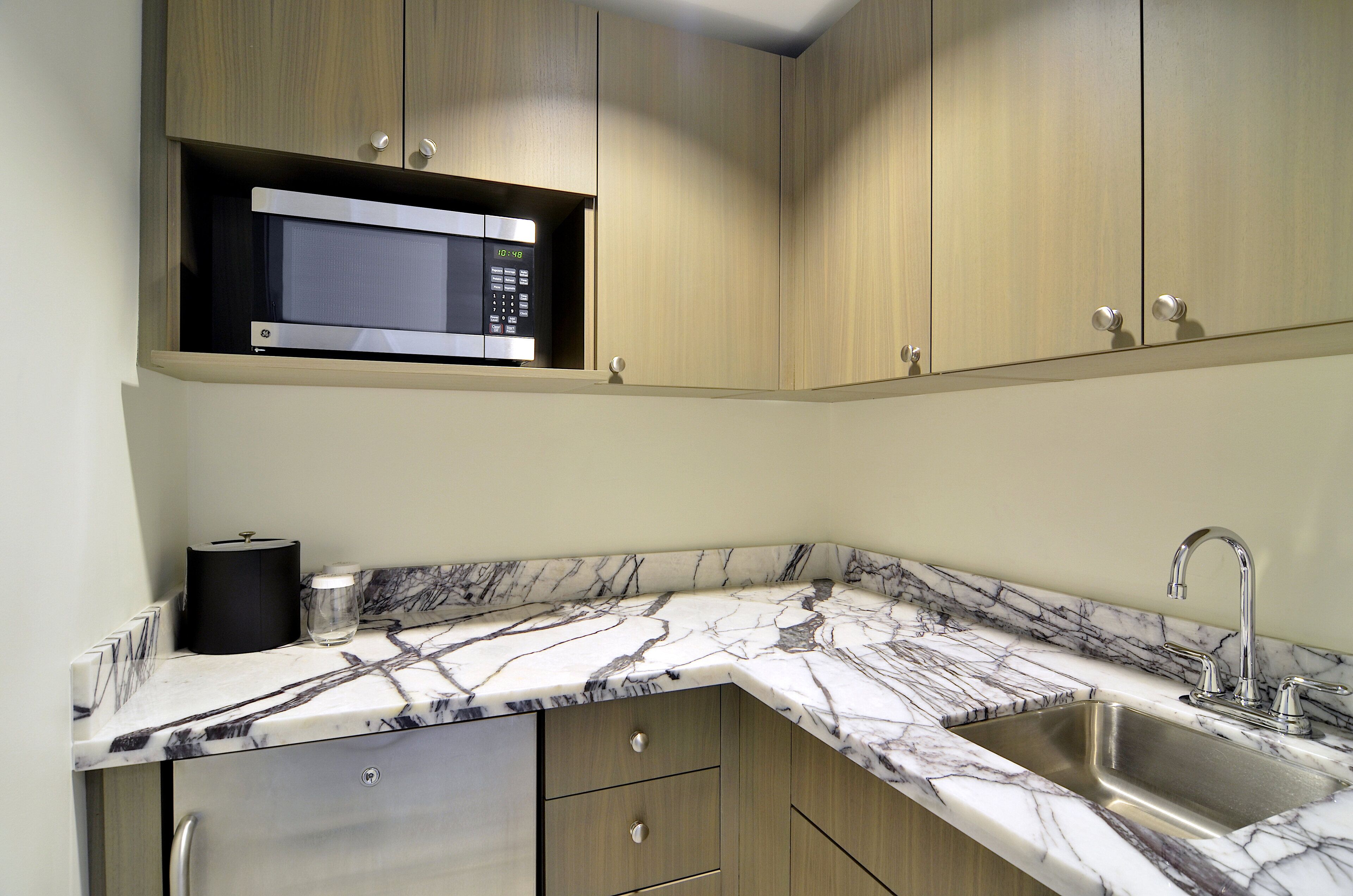 A kitchen with a built-in microwave, a sink, and marble countertops.