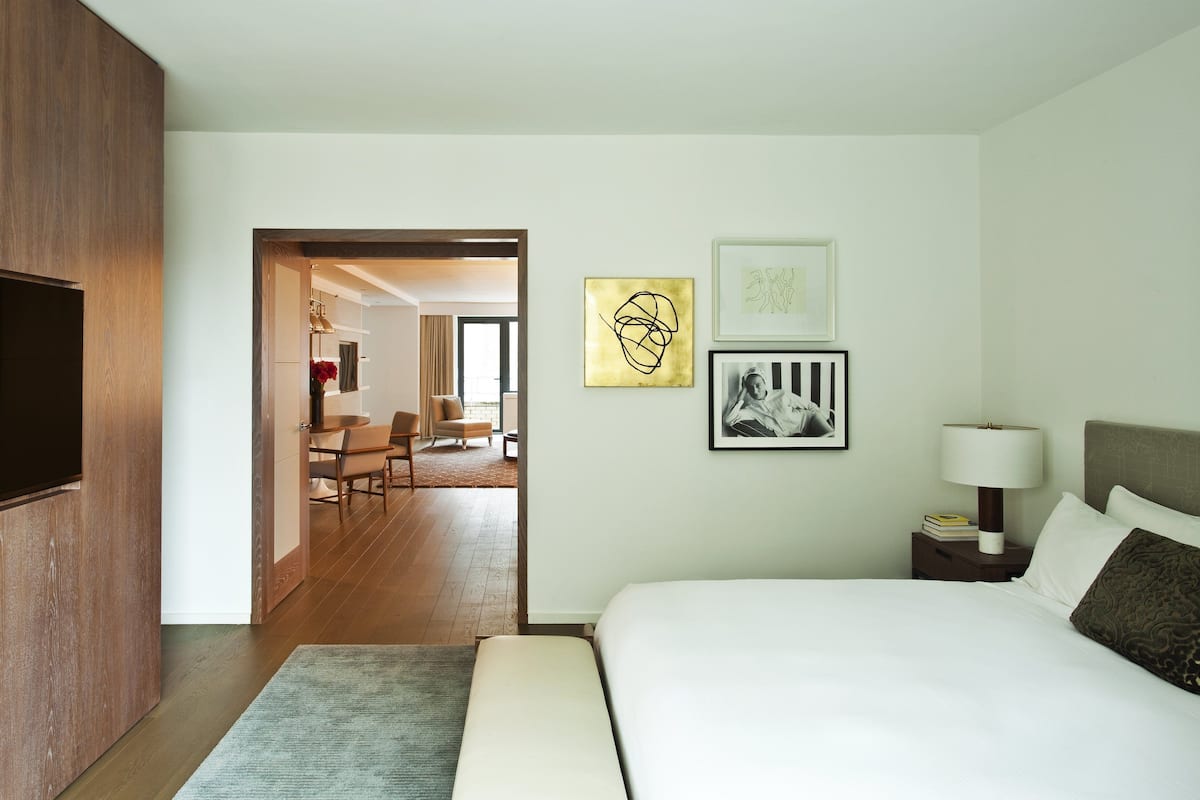 A hotel room with a bed, bedside table, lamp, and artwork on the wall.