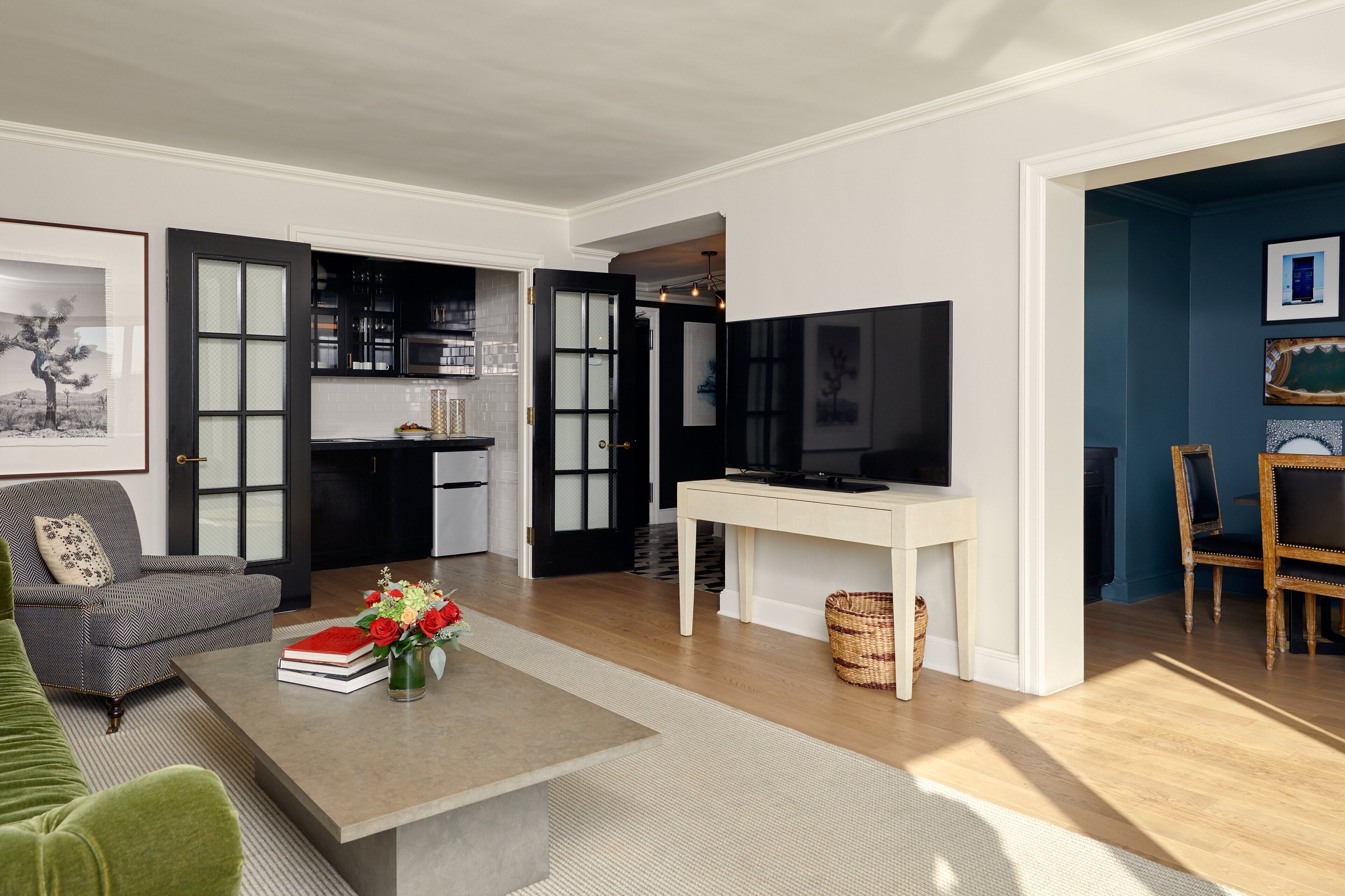 Una sala de estar moderna con sofá, mesa de centro y televisor. Se ve un área de cocina a través de una puerta abierta.