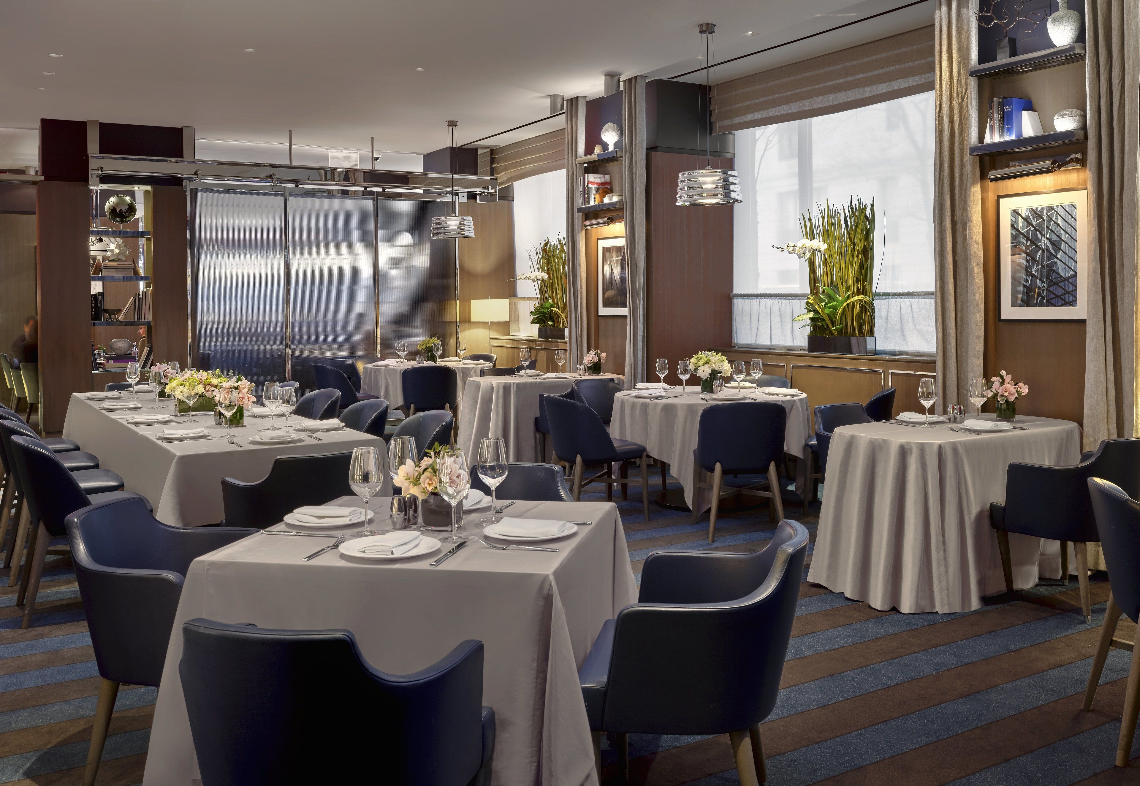 A modern dining area with multiple tables and chairs, each set with white tablecloths and wine glasses.