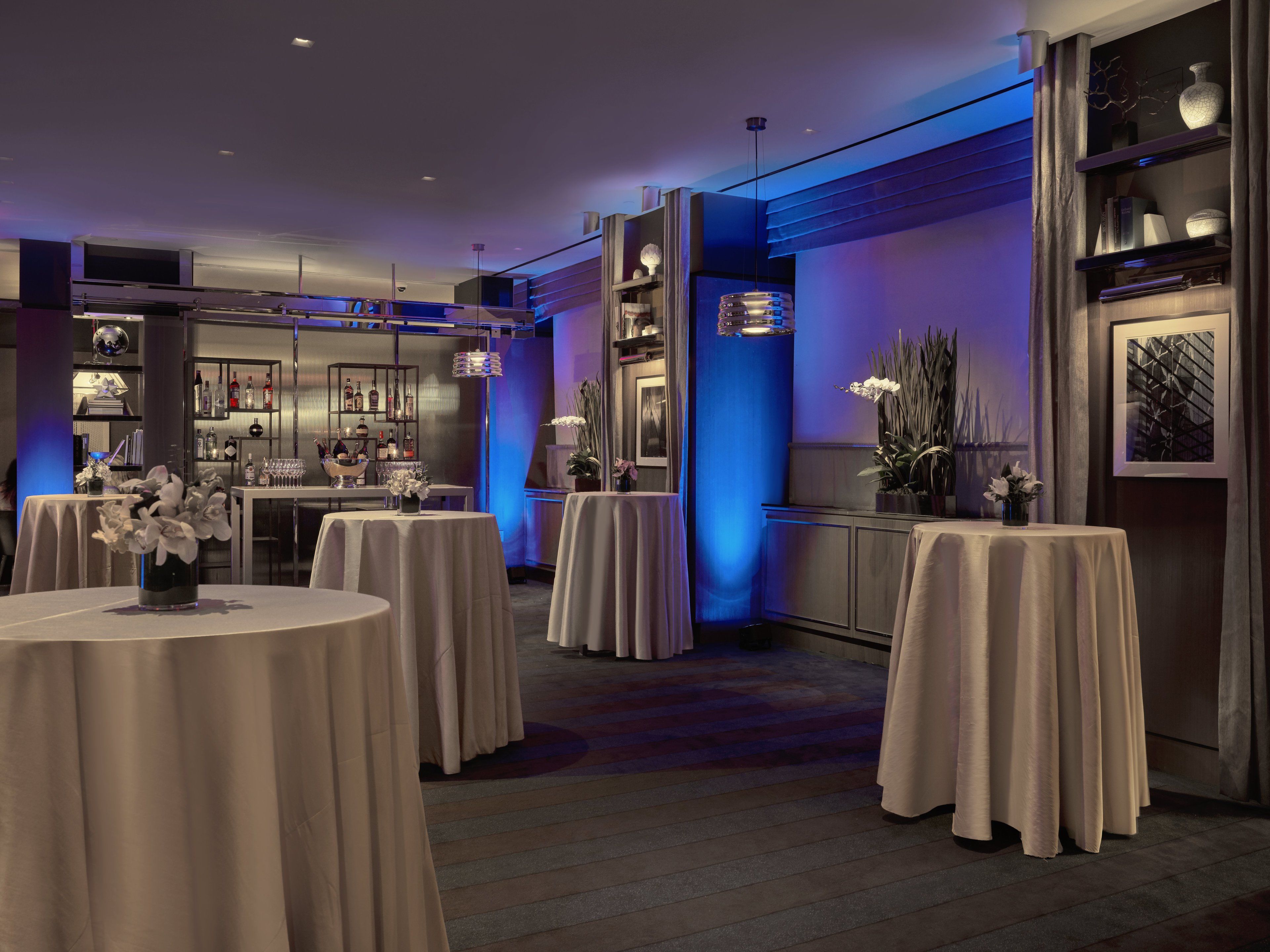 Un moderno vestíbulo de hotel con mesas redondas, una zona de bar y un mostrador de recepción.