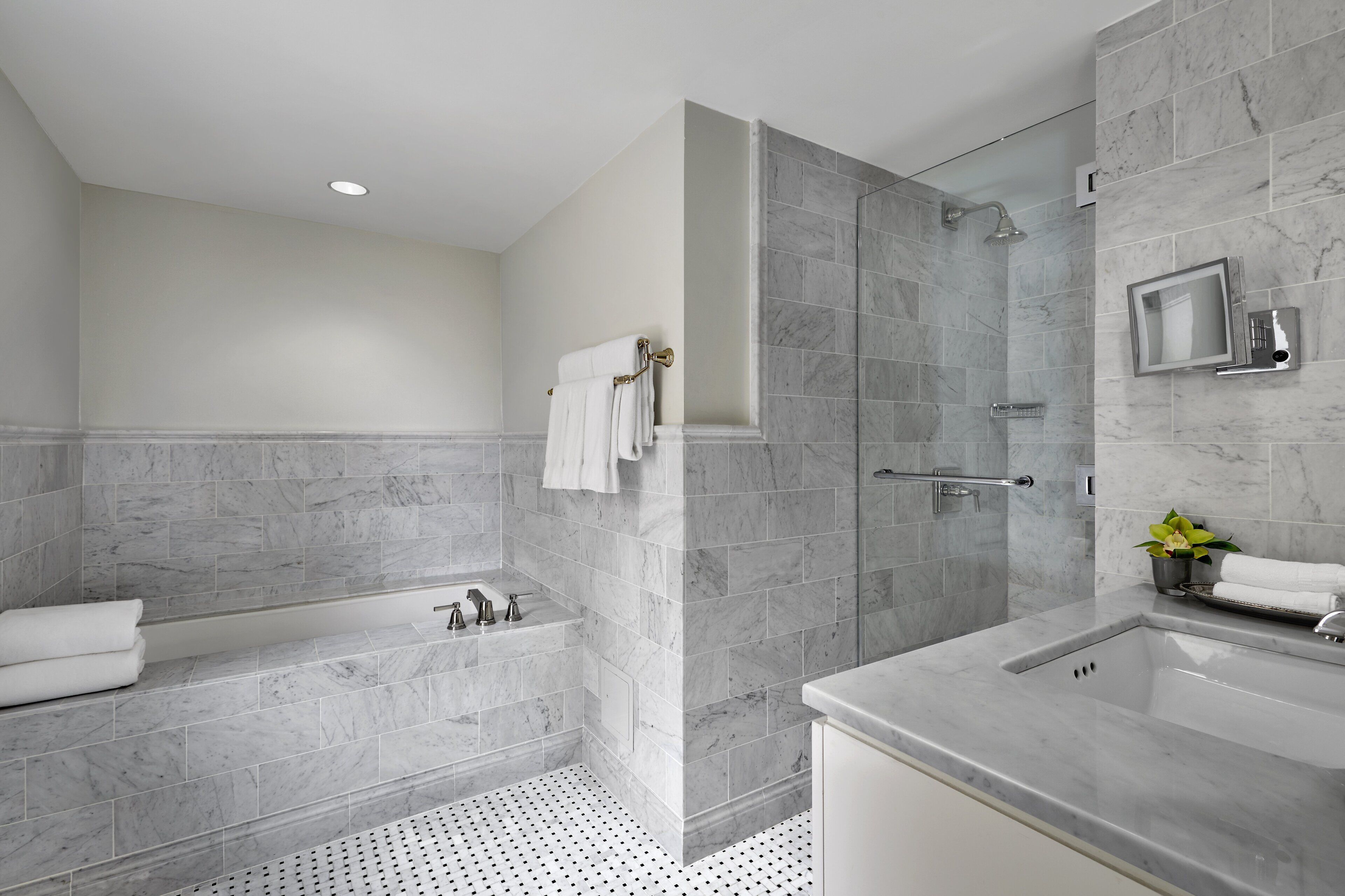 A modern bathroom with a bathtub, shower, and sink, all with marble tiling.