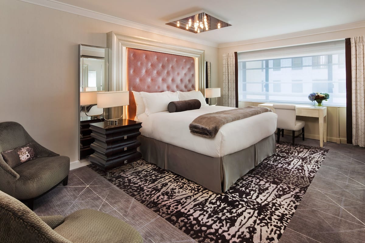A hotel room with a large bed, a desk, a chair, and a window with curtains.