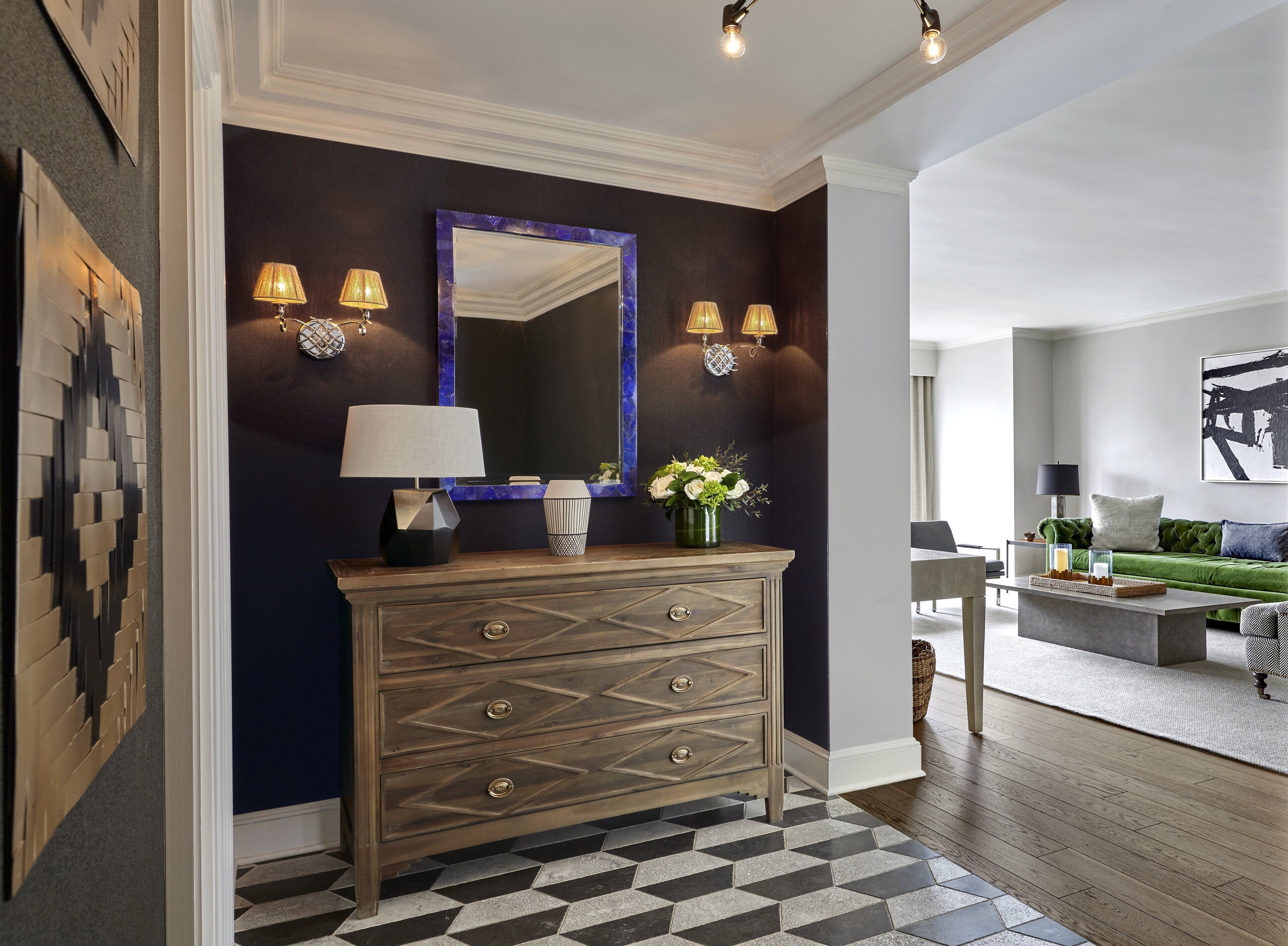 A hallway with a dark wall, a wooden dresser with drawers, a mirror, and wall sconces.
