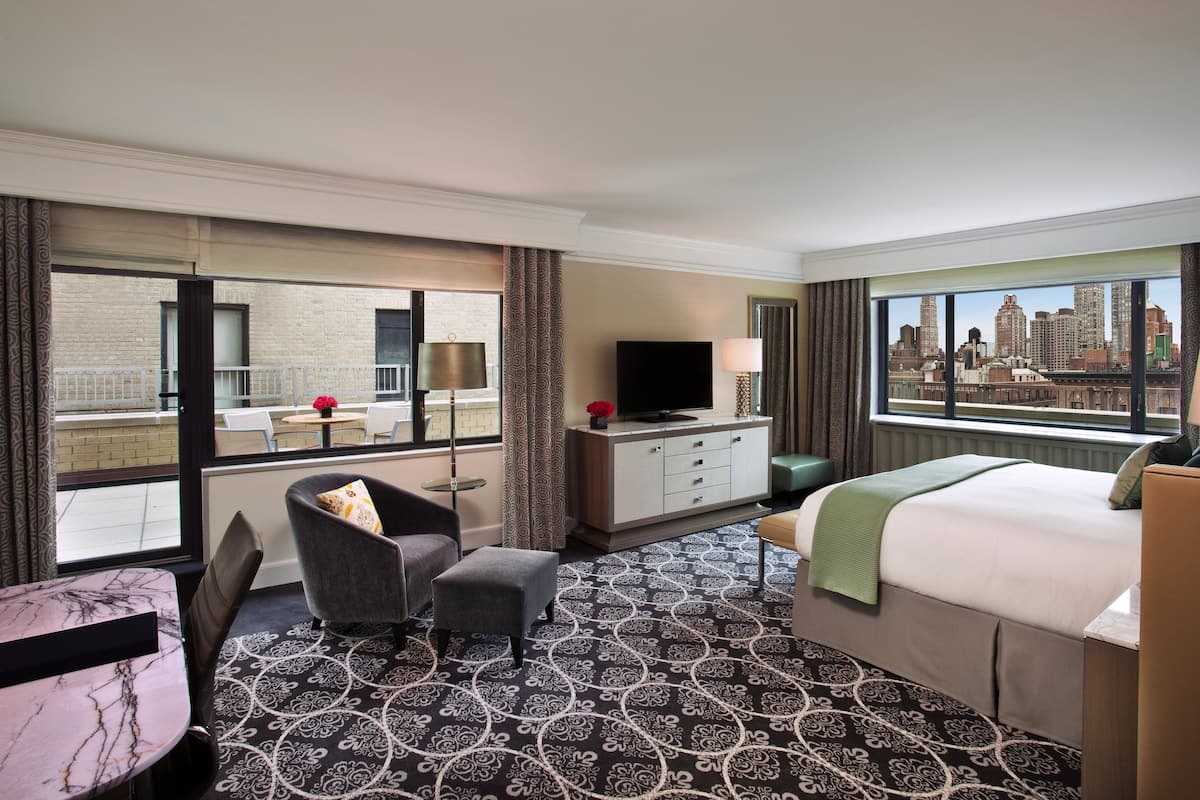 A hotel room with a large window, a bed, a TV, a desk, and a chair.