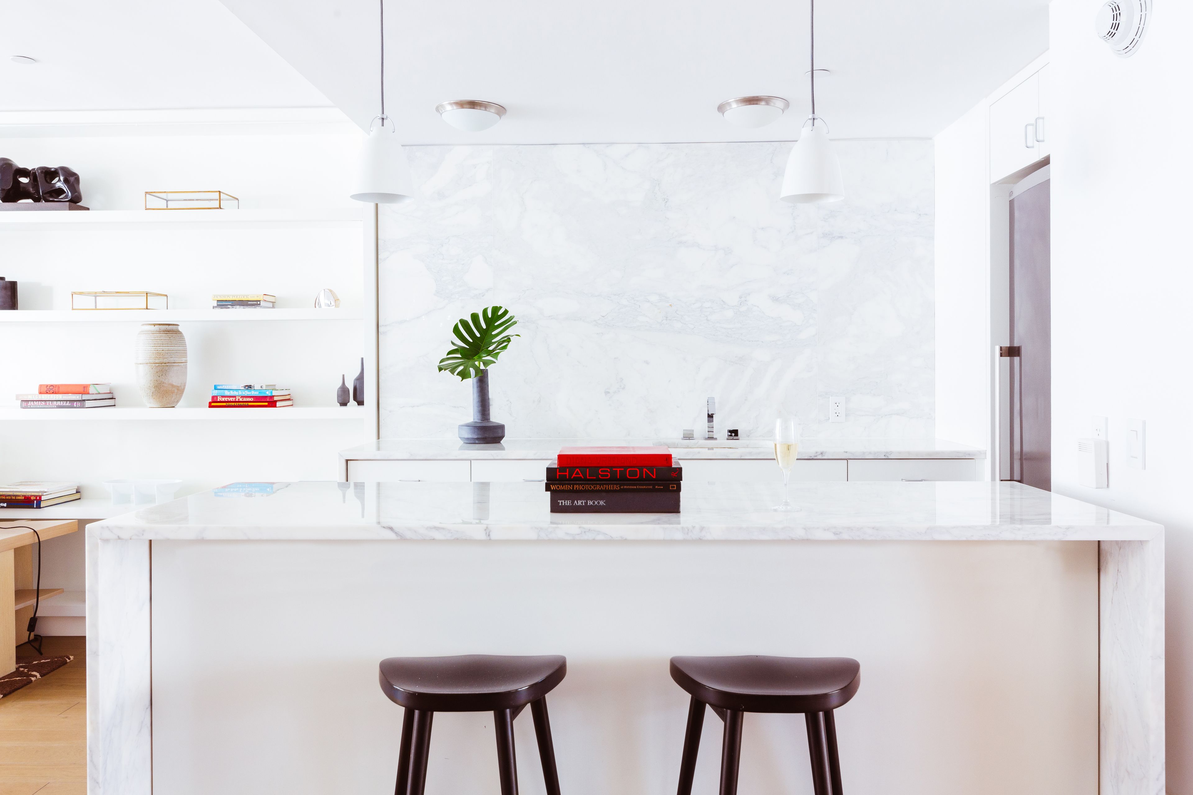 Una cocina moderna con encimera de mármol, dos taburetes de bar y una planta en maceta.