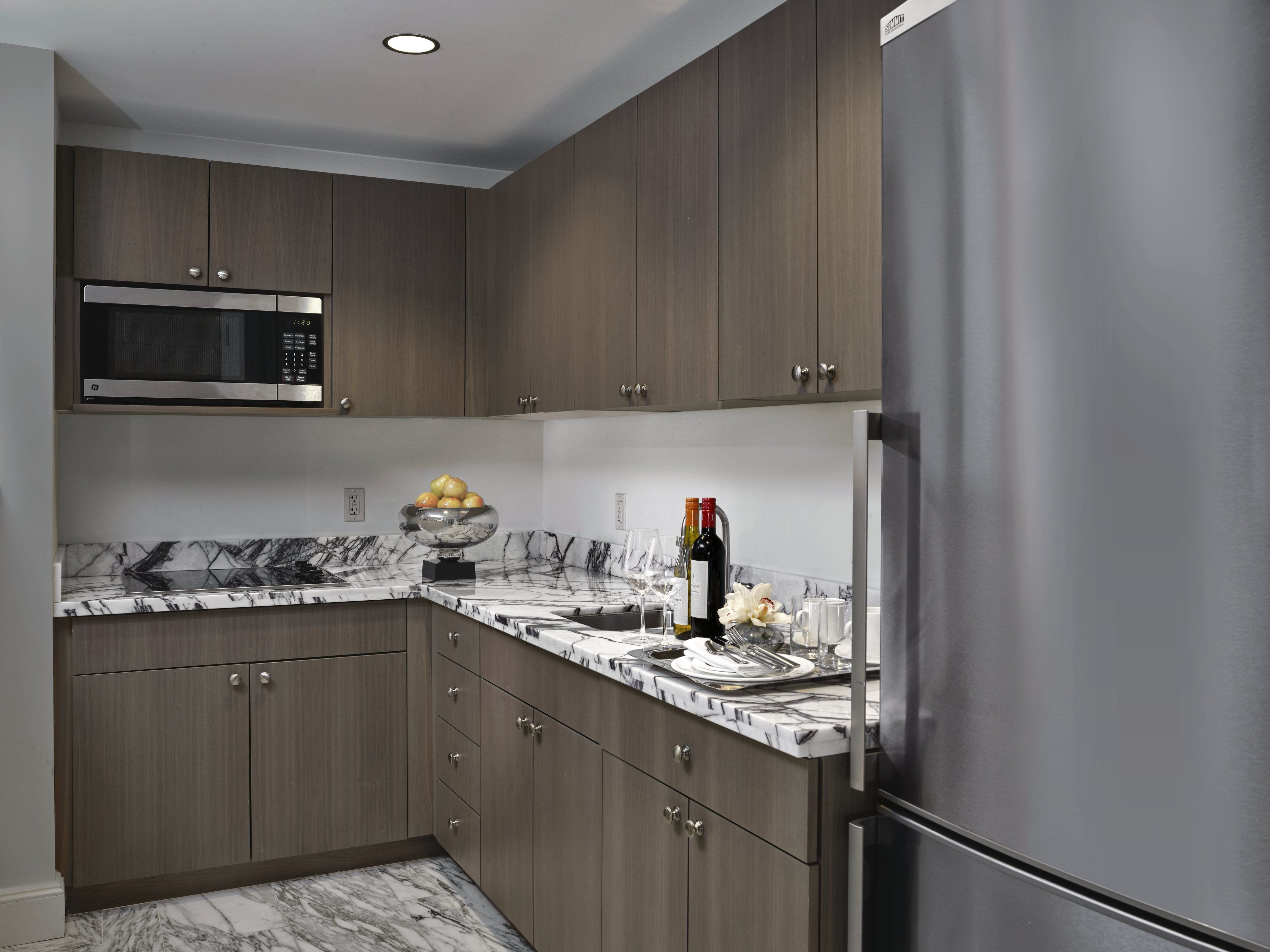 Una cocina moderna con armarios de madera oscura, un refrigerador de acero inoxidable, un microondas y una encimera de mármol.