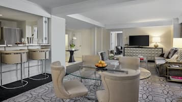 A modern hotel room with a dining area, a sofa set, a TV, and a lamp.