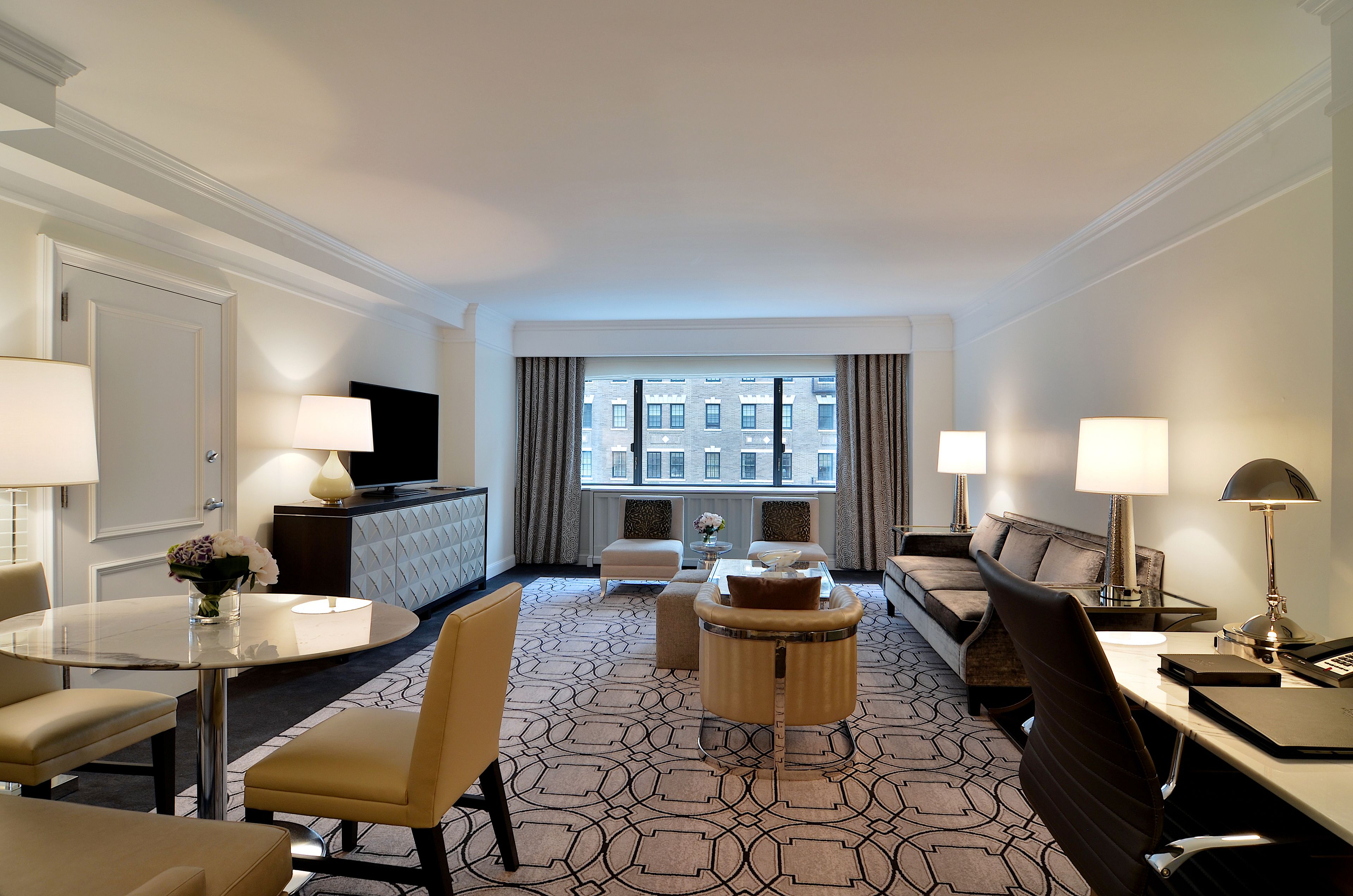 A hotel room with a round table, two armchairs, a sofa, a coffee table, and a TV.