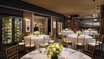 Un salón de banquetes con mesas redondas dispuestas para comer, con manteles blancos, sillas doradas y centros de mesa florales.