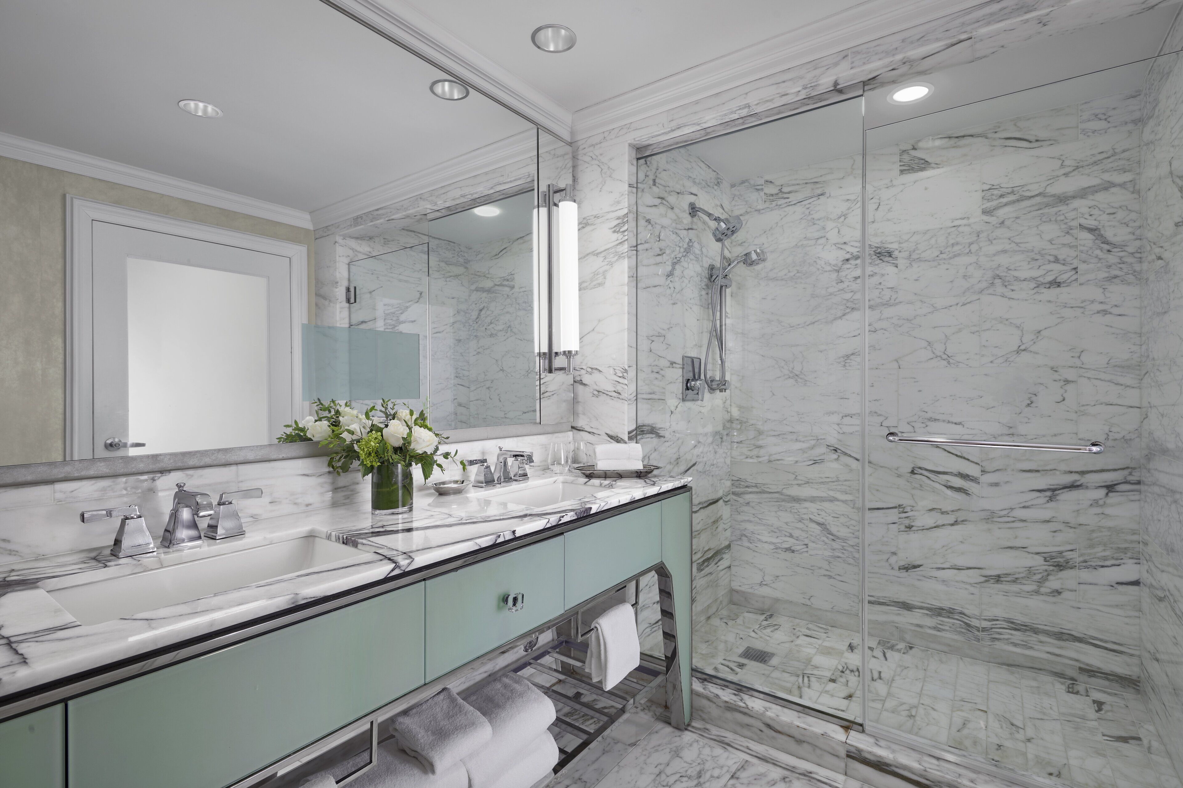 A modern bathroom with a marble sink, a glass shower enclosure, and a large mirror.