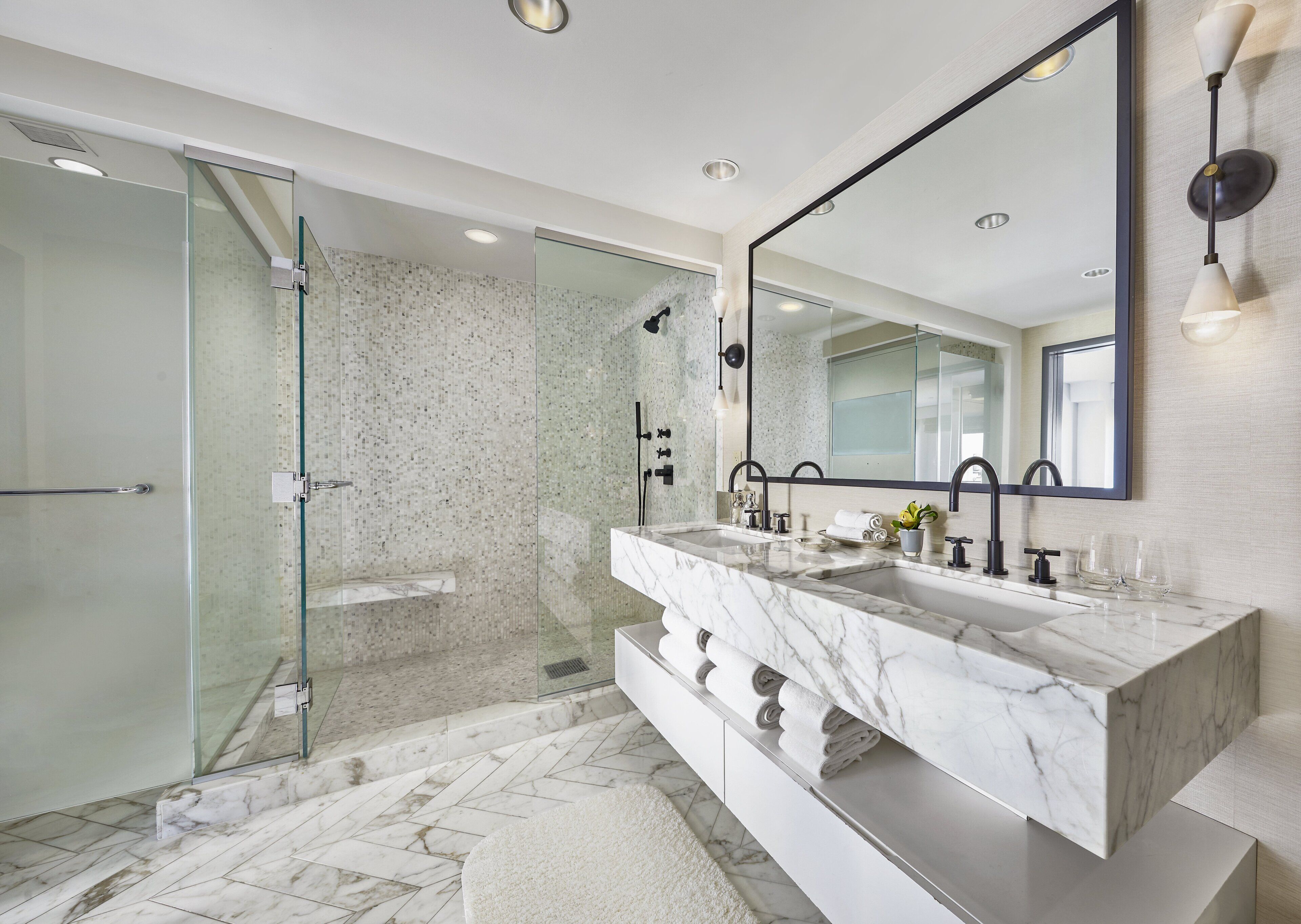 Une salle de bain moderne avec une douche à parois de verre, un grand miroir et un meuble-lavabo en marbre.